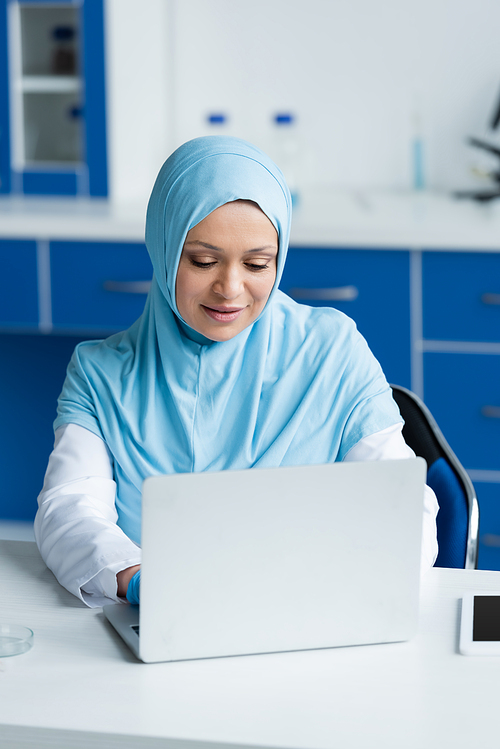 Muslim scientist using laptop near digital tablet and petri dish