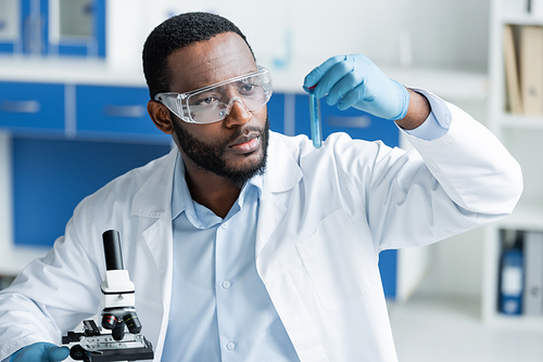 African american scientist in goggles holding test tube near microscope in laboratory