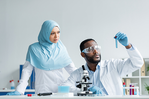 Interracial scientists in latex gloves looking at sample near microscope in laboratory