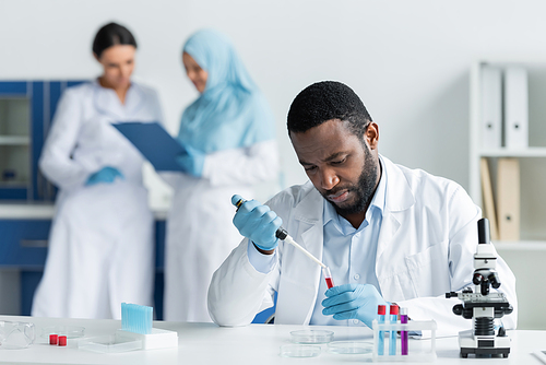 African american scientist researching samples in test tubes near blurred colleagues in lab