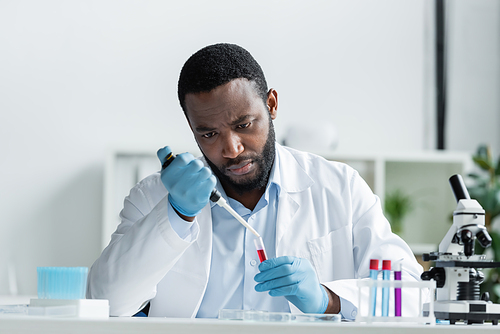 African american scientist in latex gloves holding test tube and electronic pipette in laboratory