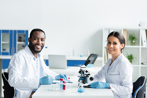 Smiling multiethnic scientists looking at camera near medical equipment