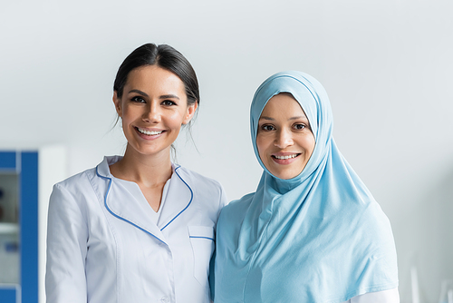 Smiling doctor looking at camera near muslim colleague in clinic