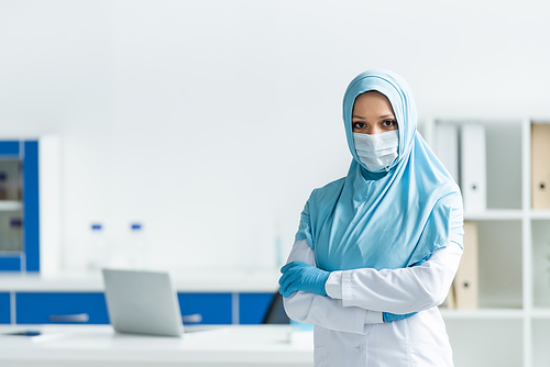 Muslim doctor in medical mask and hijab standing with crossed arms in clinic