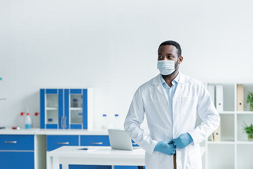 African american scientist in medical mask adjusting white coat in lab