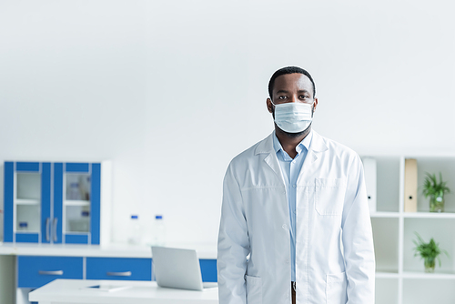 African american scientist in medical mask and white coat looking at camera