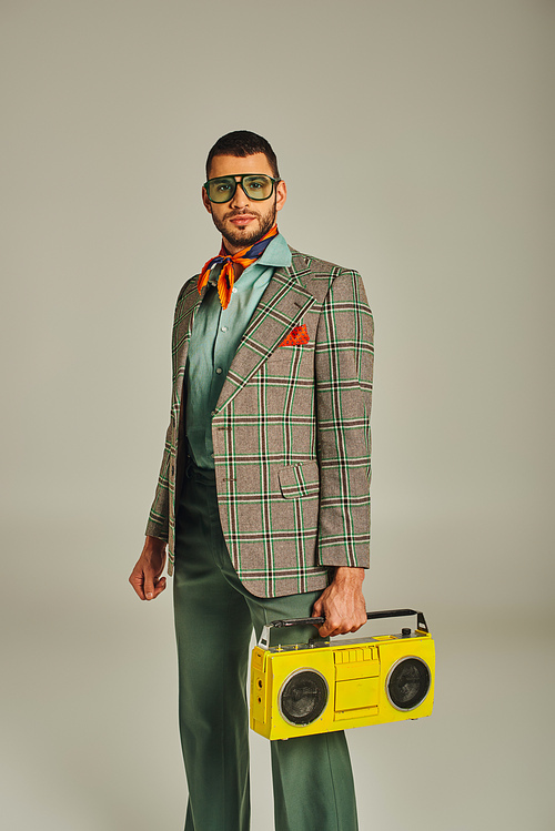 trendy man in plaid blazer and sunglasses holding yellow boombox on grey, retro-inspired lifestyle