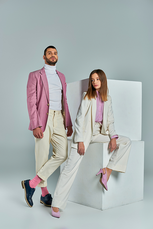 modern couple in pastel business attire posing near white cubes on grey, young professionals