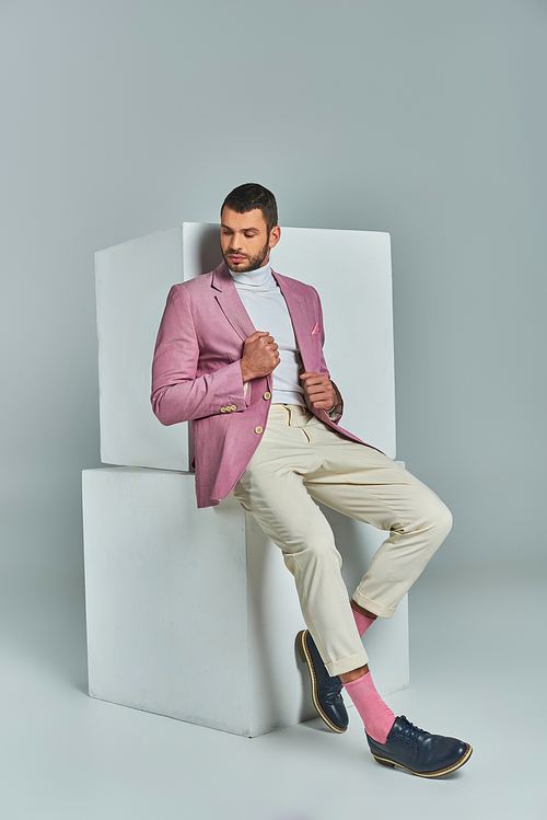 full length of trendy man in pastel purple blazer and white pants posing near cubes on grey backdrop