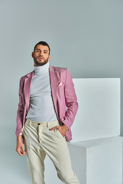 confident man in lilac blazer posing with hand in pocket near white cubes on grey, business fashion