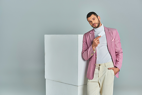 trendy man in lilac blazer posing with hand in pocket and blank business card near cubes on grey