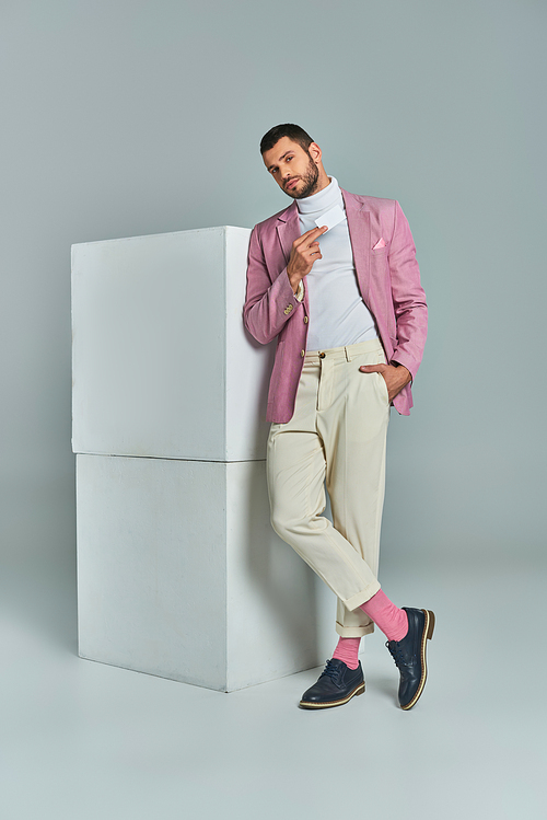 stylish man in lilac blazer standing with hand in pocket and blank business card near cubes on grey