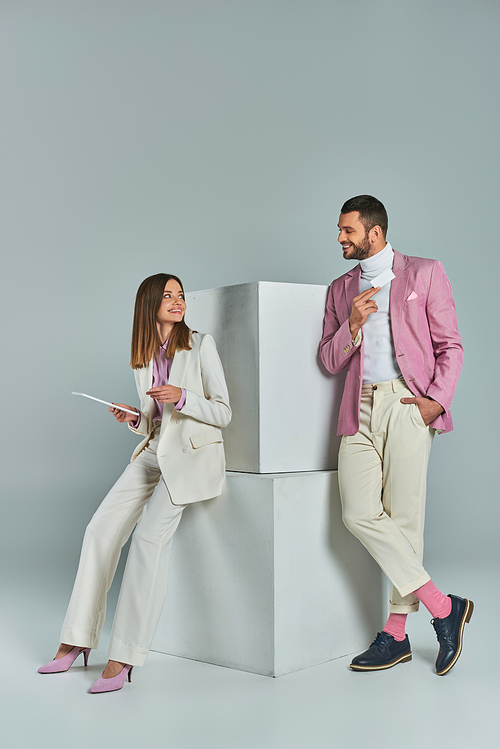 stylish couple with business card and digital tablet smiling at each other near cubes on grey