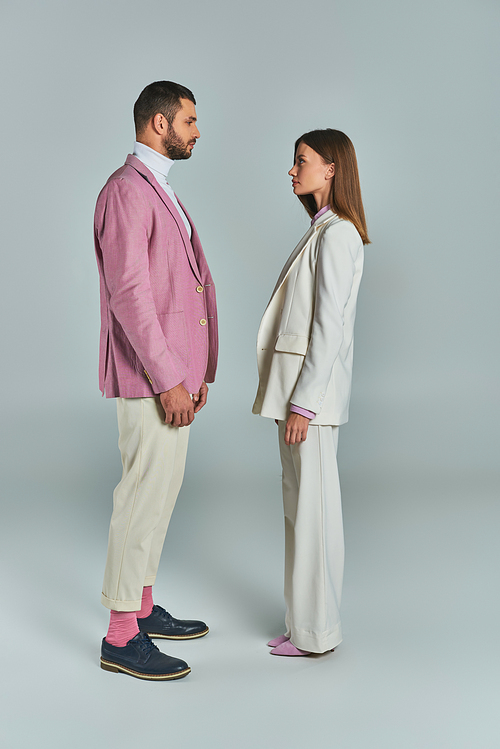 full length of young couple in stylish suits looking at each other on grey, modern business fashion