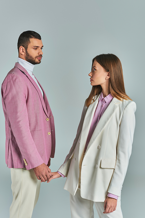 young fashionable couple in pastel business attire holding hand and looking at each other on grey