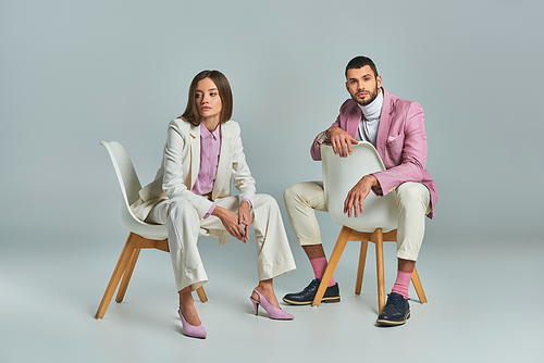 trendy business couple in pastel formal wear sitting in armchairs on grey, minimalistic fashion