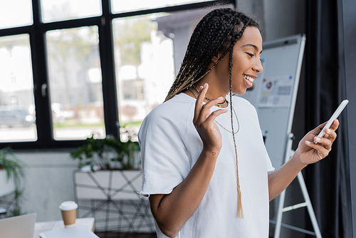 Positive african american businesswoman in t-shirt having video call on smartphone in office