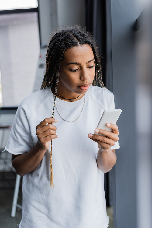 African american businesswoman in t-shirt using smartphone in blurred office