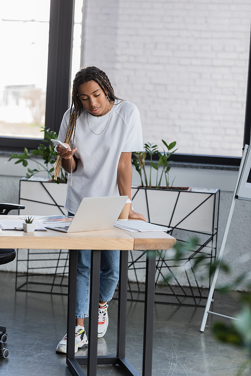 African american manager in casual clothes using gadgets near papers in modern office