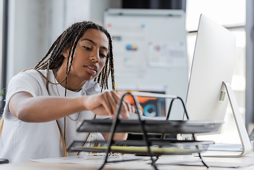 African american businesswoman taking paper near devices in office