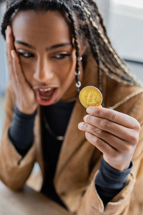 KYIV, UKRAINE - APRIL 27, 2022: Shocked african american businesswoman holding bitcoin