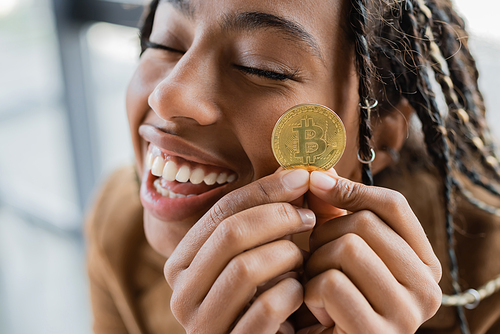 KYIV, UKRAINE - APRIL 27, 2022: Positive african american businesswoman holding golden bitcoin in office