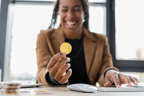 KYIV, UKRAINE - APRIL 27, 2022: Blurred african american businesswoman holding bitcoin near computer keyboard in office