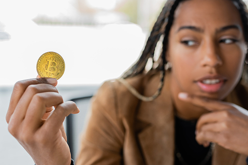 KYIV, UKRAINE - APRIL 27, 2022: Blurred african american businesswoman looking at bitcoin in office