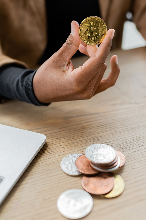 KYIV, UKRAINE - APRIL 27, 2022: Cropped view of african american businesswoman holding cryptocurrency near laptop in office