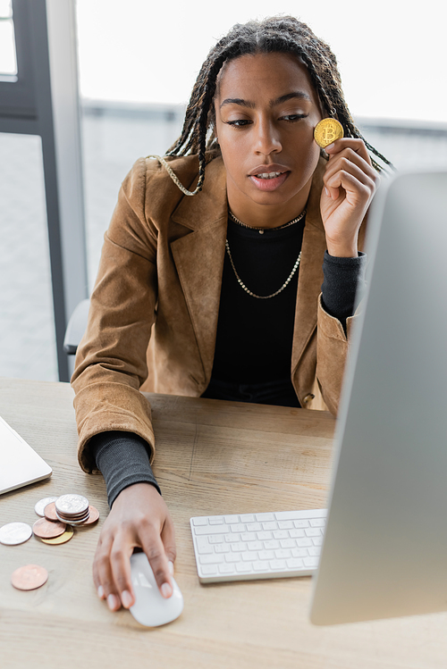 KYIV, UKRAINE - APRIL 27, 2022: African american businesswoman holding bitcoin and using computer in office