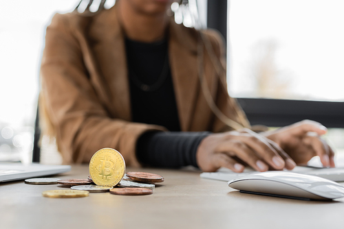 KYIV, UKRAINE - APRIL 27, 2022: Cropped view of bitcoins near blurred african american businesswoman typing on computer keyboard