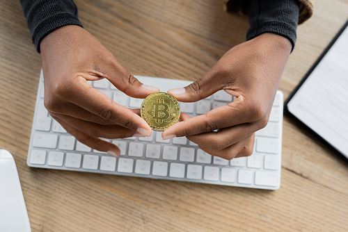 KYIV, UKRAINE - APRIL 27, 2022: Cropped view of african american businesswoman holding bitcoin near blurred computer keyboard in office