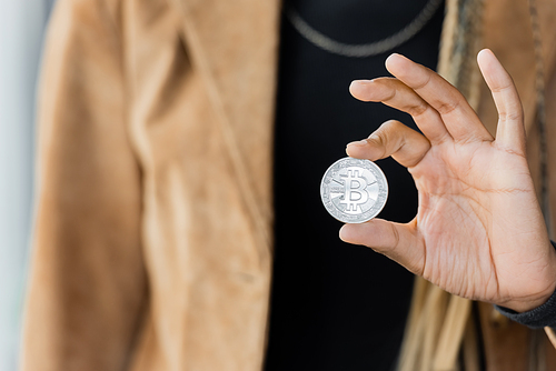 KYIV, UKRAINE - APRIL 27, 2022: Cropped view of blurred african american businesswoman holding silver bitcoin