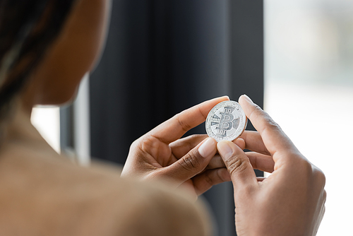 KYIV, UKRAINE - APRIL 27, 2022: Cropped view of blurred african american businesswoman holding silver bitcoin in office