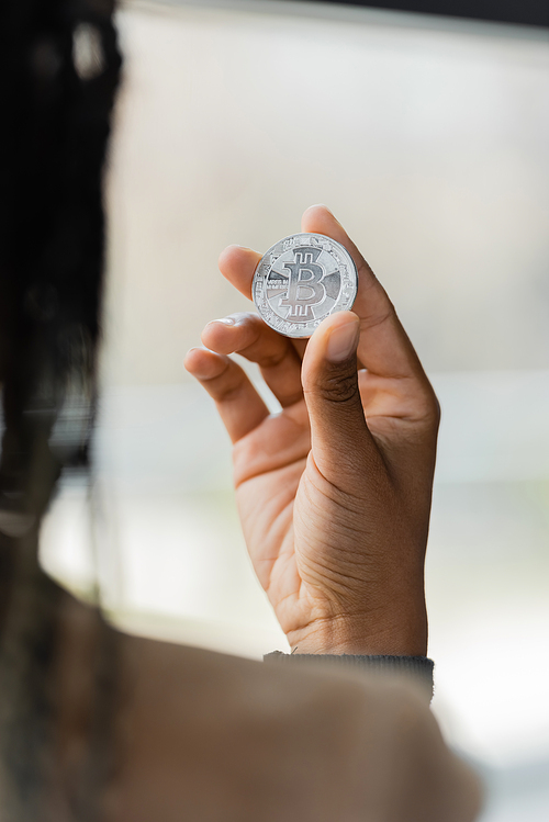 KYIV, UKRAINE - APRIL 27, 2022: Blurred african american businesswoman holding silver bitcoin in office