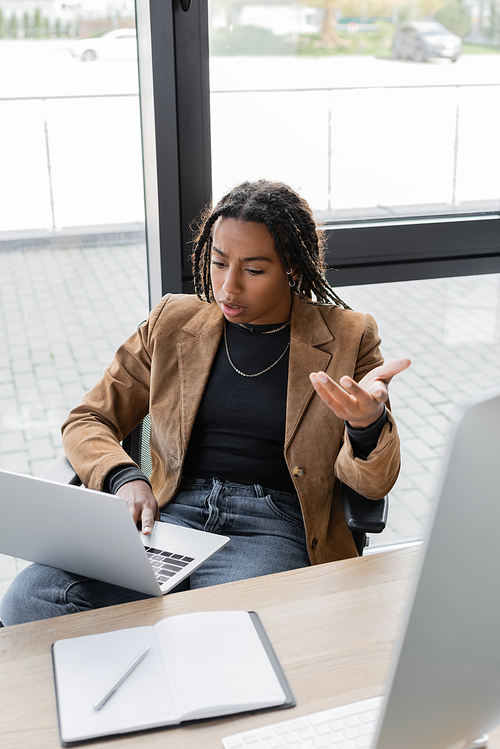 African american businesswoman having video call on laptop near notebook on table in office