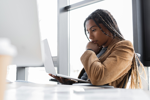 African american businesswoman in jacket holding laptop in office