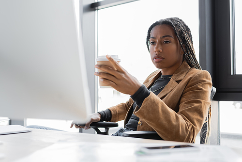 African american businesswoman holding coffee to go near computer in office