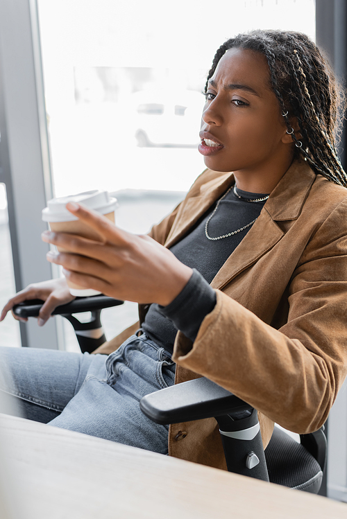 African american businesswoman in jacket holding coffee to go in office