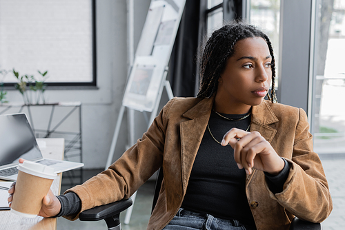 African american businesswoman in jacket holding coffee to go in office