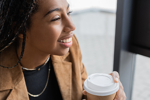 Smiling african american businesswoman in jacket holding paper cup in office