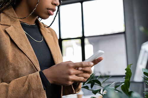 Cropped view of african american businesswoman in blazer using cellphone in office