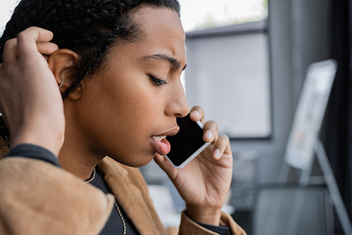 Side view of serious african american businesswoman talking on smartphone in office