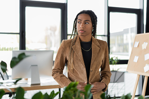 African american businesswoman in jacket looking away in blurred office