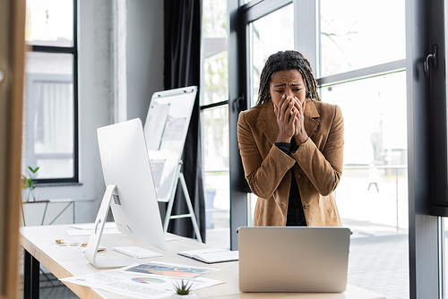 Stressed african american businesswoman looking at laptop near documents in office