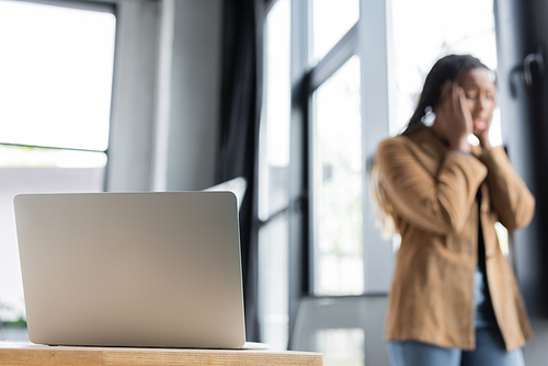 Laptop on table near blurred african american businesswoman in office