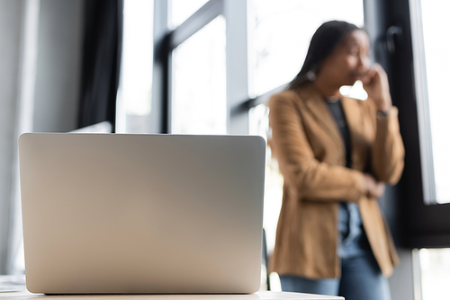 Laptop near blurred african american manager standing in office