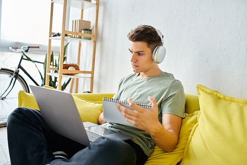 confident student with headphones in yellow couch studying in laptop and reading in note