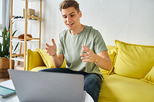 cheerful student in yellow couch with laptop on coffee table pleased speaking to online meeting