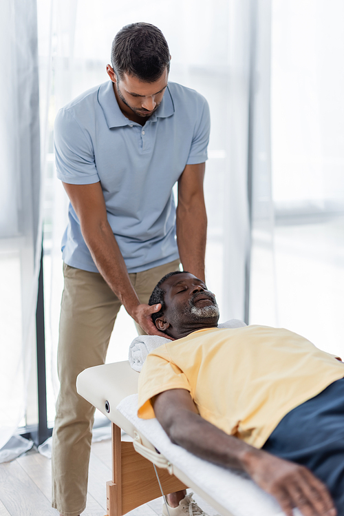 young physical therapist treating mature african american man on massage table